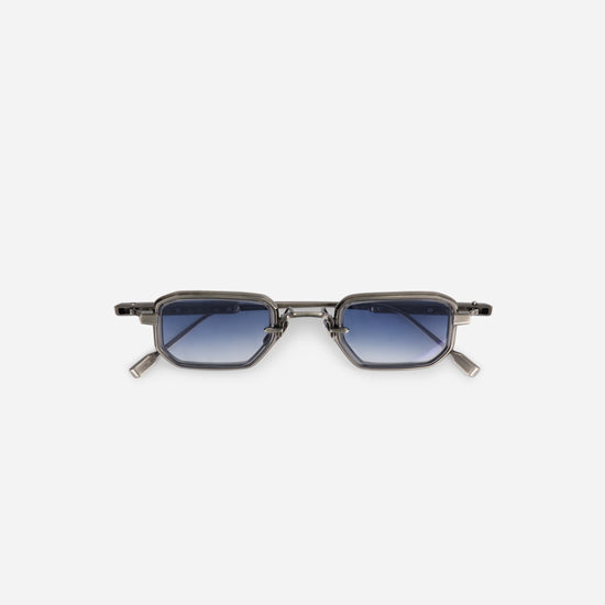 The Deneb-T AS-1, made in Japan, features a titanium frame with an antique silver coating and crystal grey rim inserts. It is paired with gradient blue lenses.