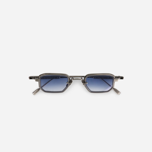 The Deneb-T AS-1, made in Japan, features a titanium frame with an antique silver coating and crystal grey rim inserts. It is paired with gradient blue lenses.