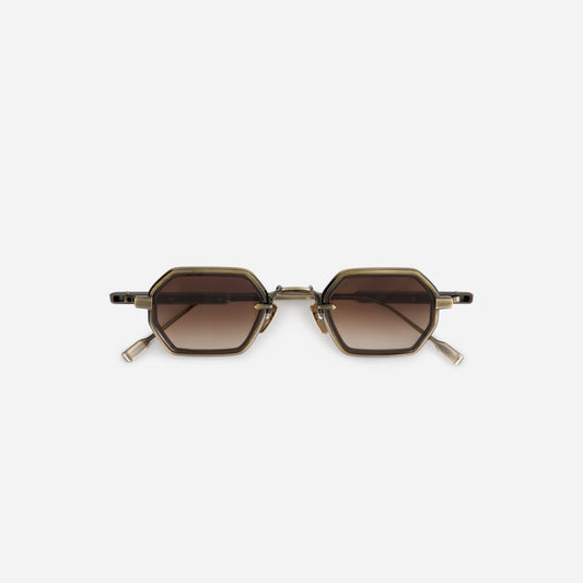 The Hadar-T AG/AS-1 is a stylish eyewear featuring a titanium frame with an antique gold and antique silver coating. It's complemented by a chocolate takiron rim insert and boasts gradient brown lenses for a sophisticated look.