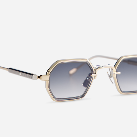 The Hadar-T LG/P-1 eyeglasses possess a titanium frame featuring lunar gold and platinum coating, complemented by a crystal grey takiron rim insert and gradient grey lenses.