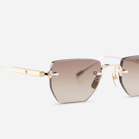 Close-up side view of rimless sunglasses with a gradient brown lens and gold titanium frame on a light gray background.