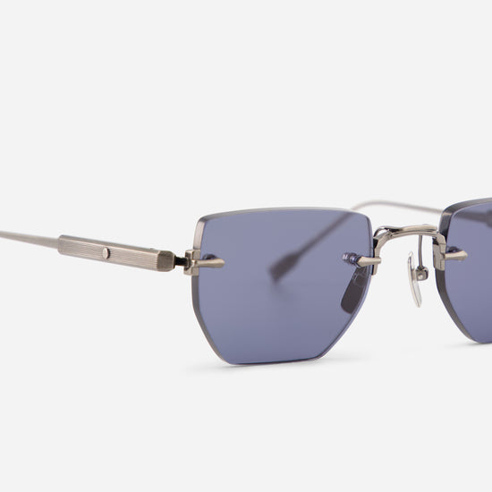 Close-up of rimless square sunglasses with dark blue lenses and antique silver titanium frames on a light gray background.