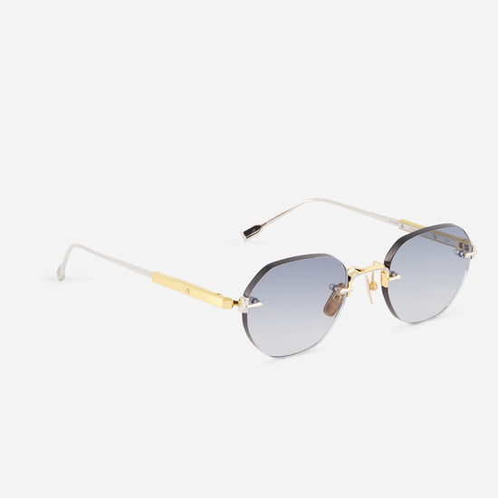Rimless sunglasses with gradient gray-blue lenses, gold metal hardware, and white temples on a light gray background.