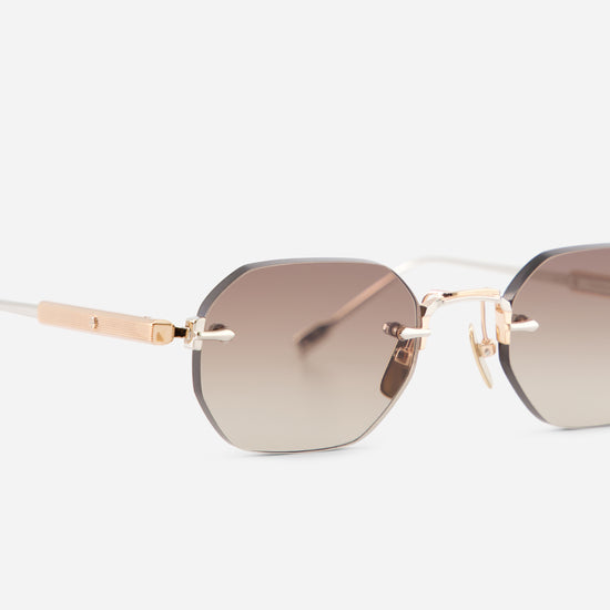 Close-up of a pair of rimless sunglasses with a geometric octagonal shape, featuring a brown gradient lens and rose gold metal frames.