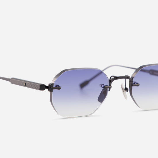 Close-up of a pair of rimless eyeglasses with a dark gray metal frame and gradient blue-to-clear lenses, shown on a light gray background.