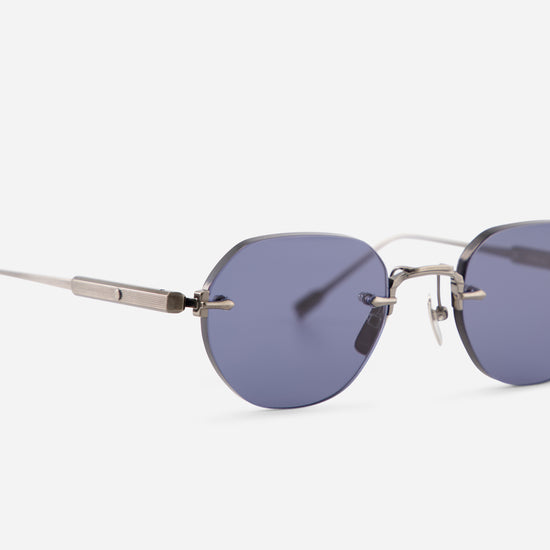 Close-up of rimless sunglasses with oval blue-gray lenses and a thin silver metal frame, shown on a light gray background.